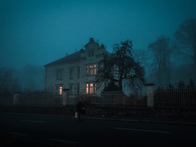 A very old mansion with a tree next to it and semi-surrounded by fog during the night for Halloween