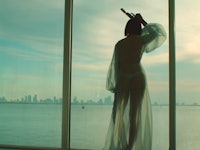 Rihanna in a sheer dress looking through a large window in her Needed Me music video