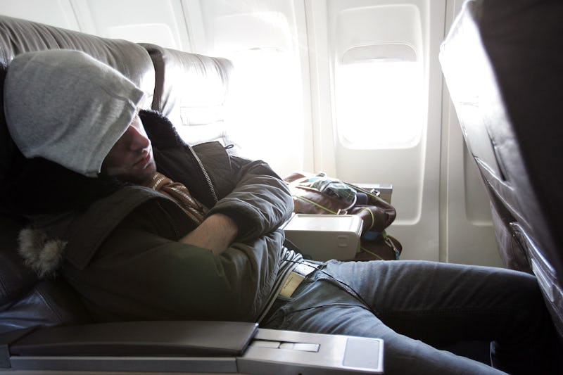 A man in a grey hoodie sleeping in an airplane seat and experiencing jet lag