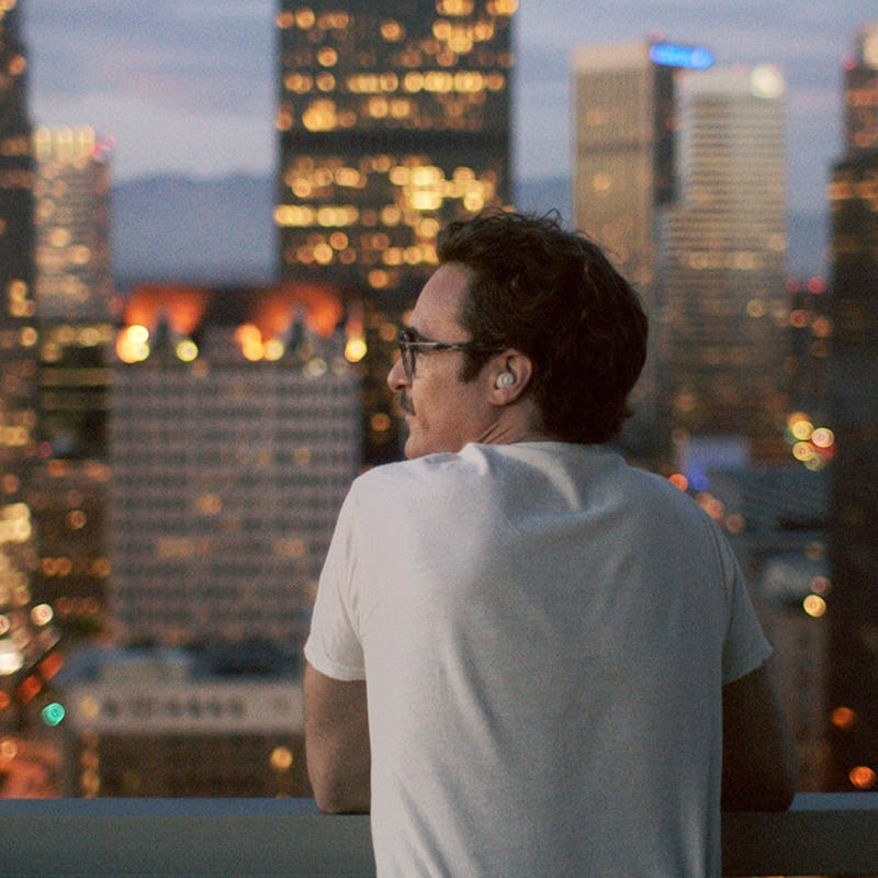 A man leaning onto a terrace fence with blurred lights of a city in the background