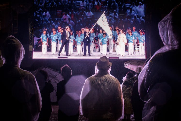 Group of people standing on the stage waving the "Olympics" flag.