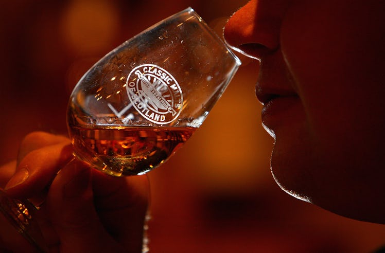 A person is smelling the whiskey from a glass.