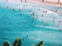 A semi-aerial view of a crowded beach and sea during Spring Break with lots of people swimming