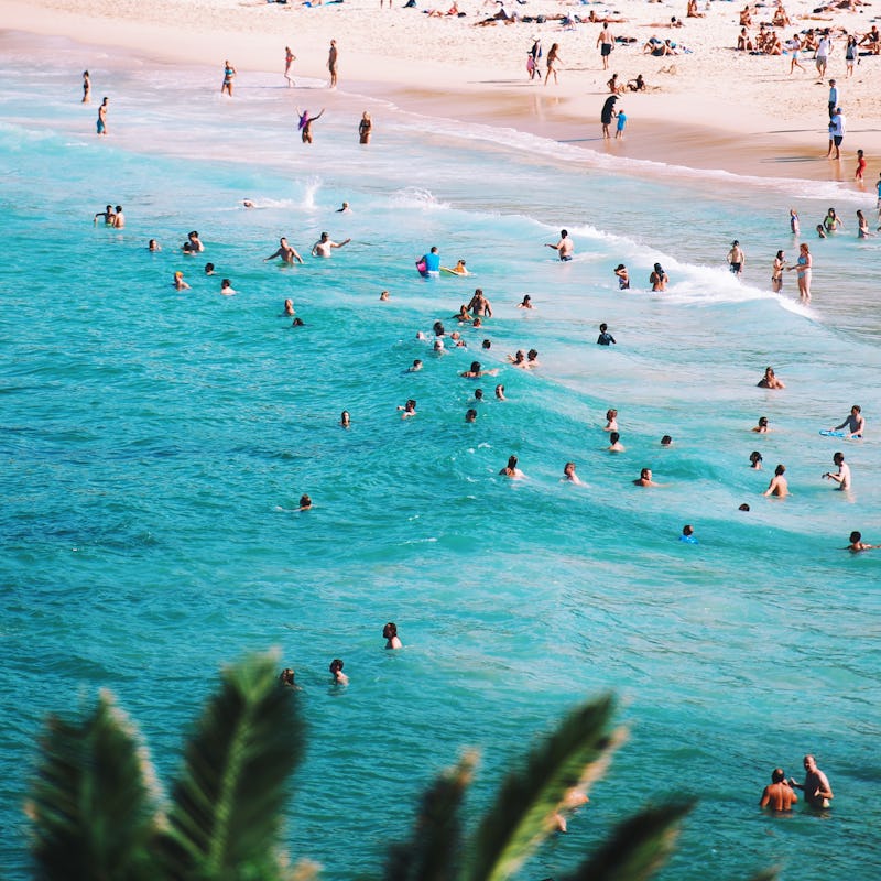 A semi-aerial view of a crowded beach and sea during Spring Break with lots of people swimming