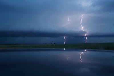 A lake on a gloomy day with lightning in the background