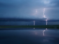 A lake on a gloomy day with lightning in the background