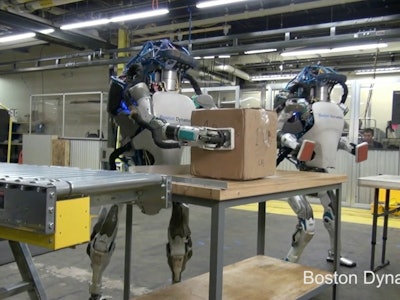Two robot workers carrying packages in a factory