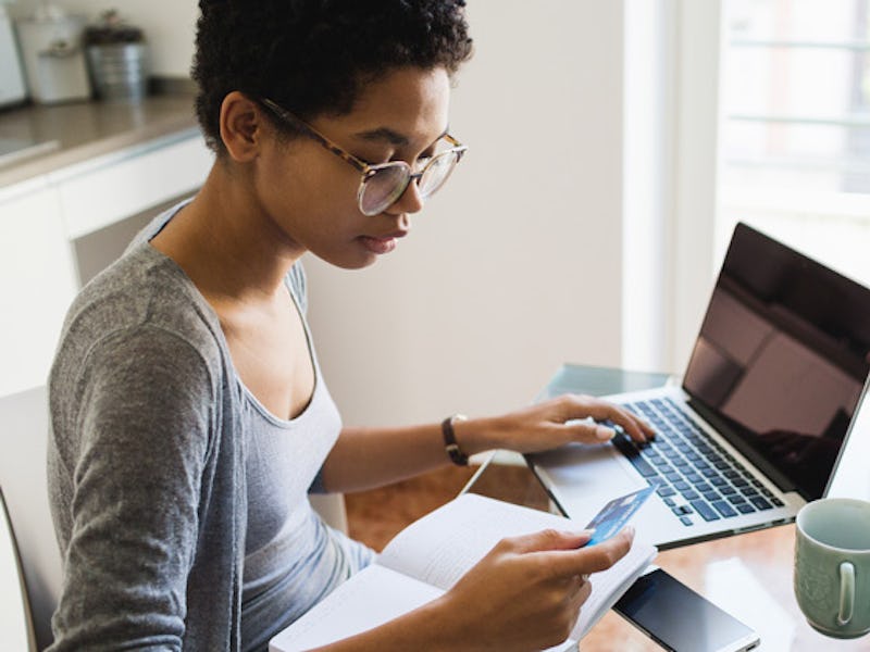 A woman sitting at a table with her laptop and credit card while paying debts off