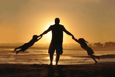 A dad with his children holding each of his arms at the beach during a sunset