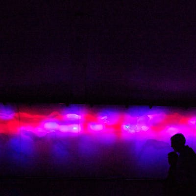 People walking next to a holographic image in purple and red