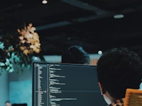 A man sitting at his computer in an office with lines of code on the screen