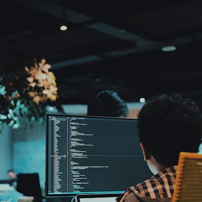 A man sitting at his computer in an office with lines of code on the screen