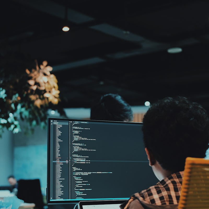 A man sitting at his computer in an office with lines of code on the screen