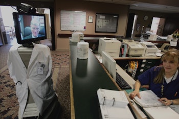 Telepresence Robot in a labcoat and with a womans face on its screen goes through the office looking...
