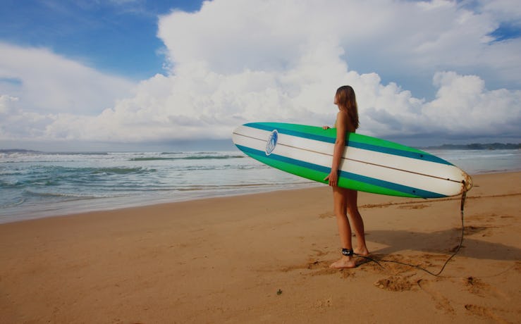 Young lady standing on a beach with a surfboard in her hands