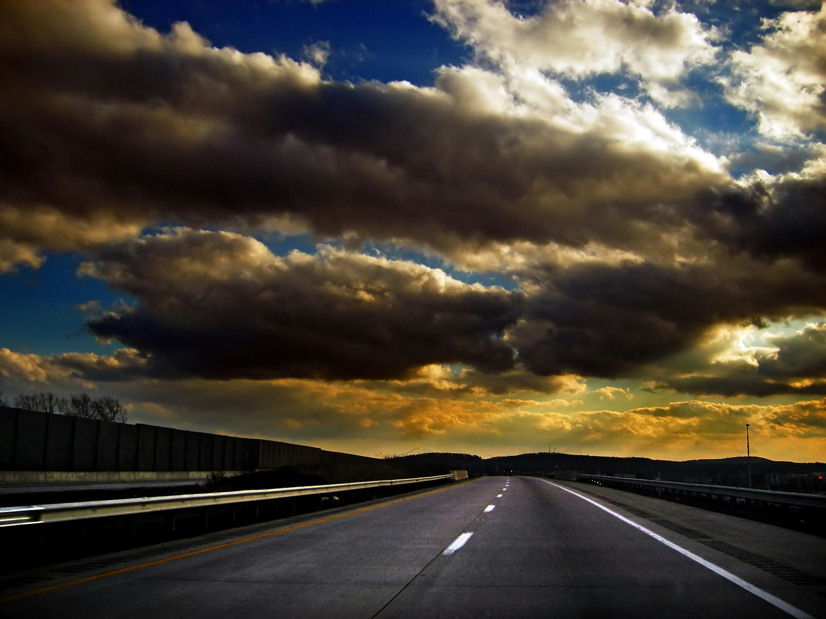 A road with accentuated clouds in yellow and white over the sky above it