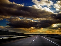 A road with accentuated clouds in yellow and white over the sky above it