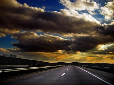 A road with accentuated clouds in yellow and white over the sky above it