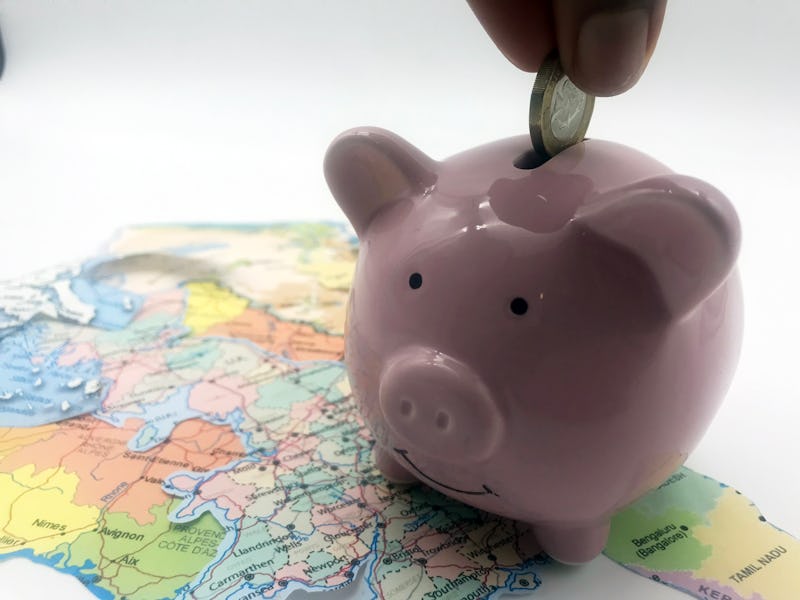 A hand dropping a coin into a piggy bank placed on a world map 