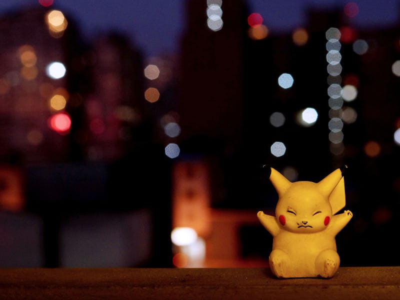 A tiny Pikachu from Pokemon Go toy next to a window with blurry city lights in the background.