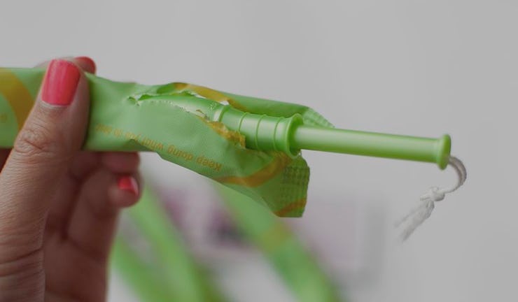 A woman with red fingernails holding a green tampon which is given out for free in Scotland