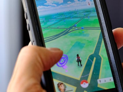 A hand holding a phone with 'Pokemon Go' game on the screen