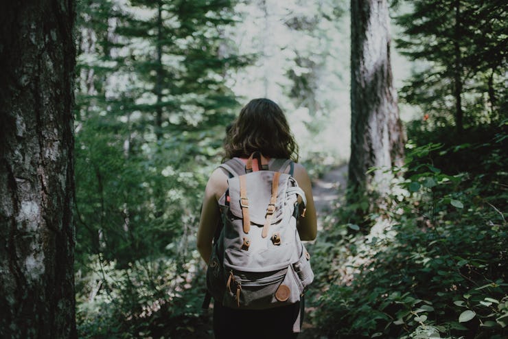 A backside photo of a girl with a backpack hiking through the woods