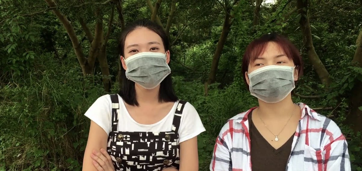 Two women standing with face masks over their mouths who know how to hack into a Tesla Model S.