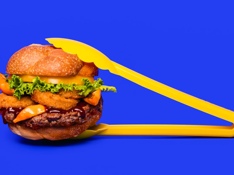 A freshly made Impossible Burger being held by yellow clamps 