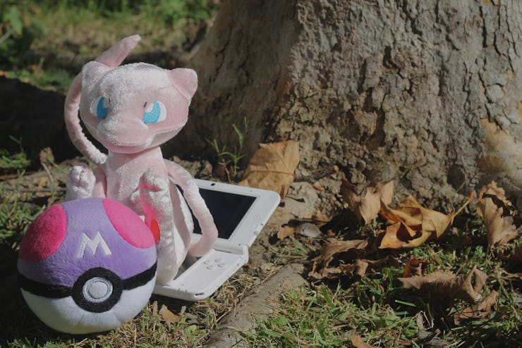 A plush Pokemon and Pokeball, and a Nintendo device placed under a tree
