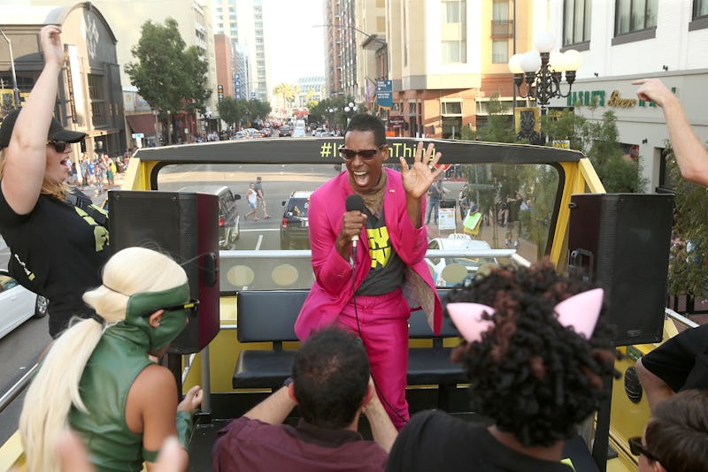 Orlando Jones in a pink suit holding a microphone while performing on the rooftop of an open bus