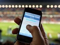 A man using his smartphone during a soccer game while a Twitter bug reveals the location of the user...