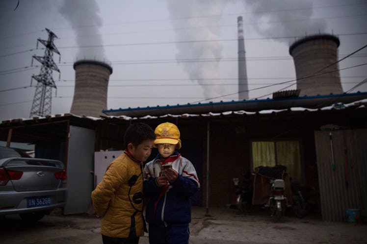 Two Asian kids are standing outside on a gloomy day, looking at the phone.