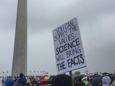 A group of people at the March for Science with a large poster and the Obelisk in the background in ...