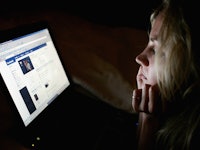 A woman sitting in the dark with the light of her laptop illuminating her face