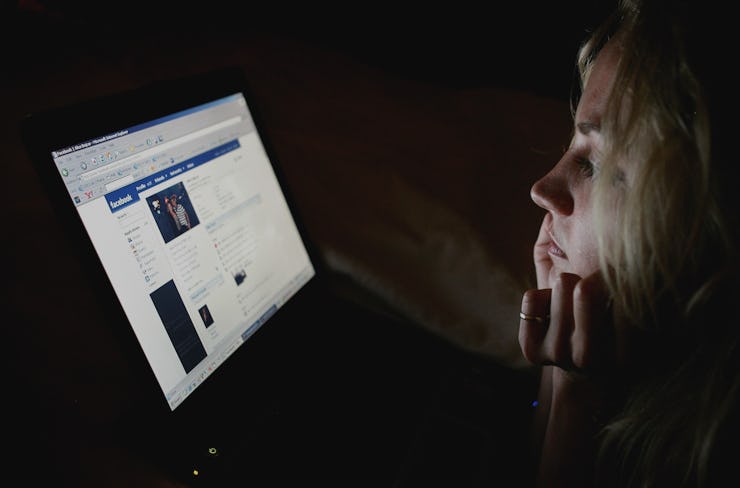 A woman sitting in the dark with the light of her laptop illuminating her face