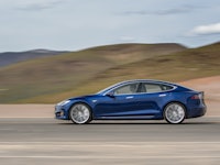 A blue tesla driving down  a desert road at high speeds