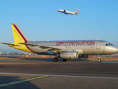 A Germanwings plane at the airport with another plane flying off in the background