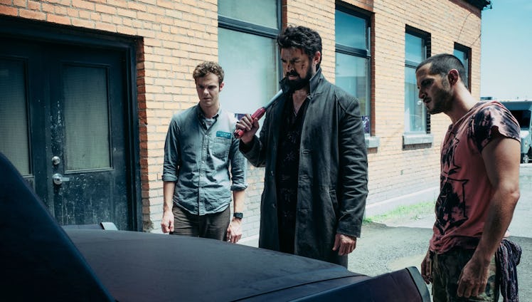 An image from "The Boys" scene where three male actors are standing beside the car