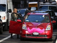 A row of cars in traffic and a woman standing next to an open door of a red car.