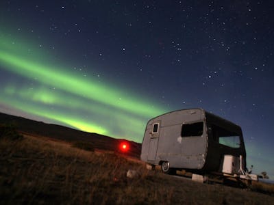 A small white SUV parked outside after a huge solar eclipse with green lights visible in the sky.