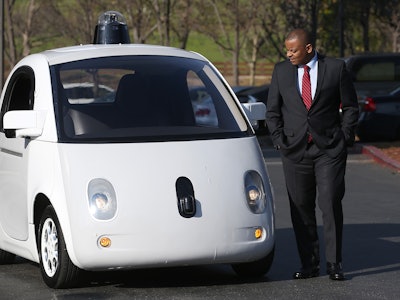 Google’s self-driving car with a driver wearing a suit while standing next to it
