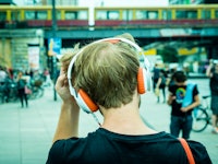 The back of a man walking through a street with headphones listening to podscasts