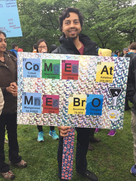 A man holding a poster with "come at me bro" text made with chemical element signs