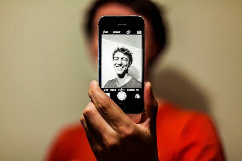 A young man smiling and taking a selfie with the back camera of his smartphone