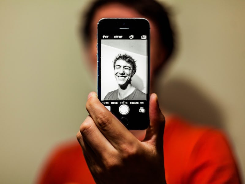 A young man smiling and taking a selfie with the back camera of his smartphone