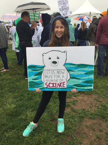 A girl holding a poster with "LET US NOW PAUSE FOR A MOMENT OF SCIENCE" text