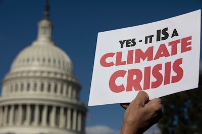 A person holding a "Yes - it is a Climate Crisis" poster and the United States Capitol in the backgr...