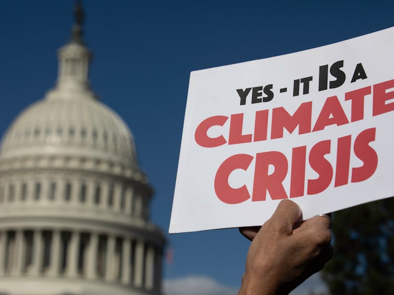 A person holding a "Yes - it is a Climate Crisis" poster and the United States Capitol in the backgr...