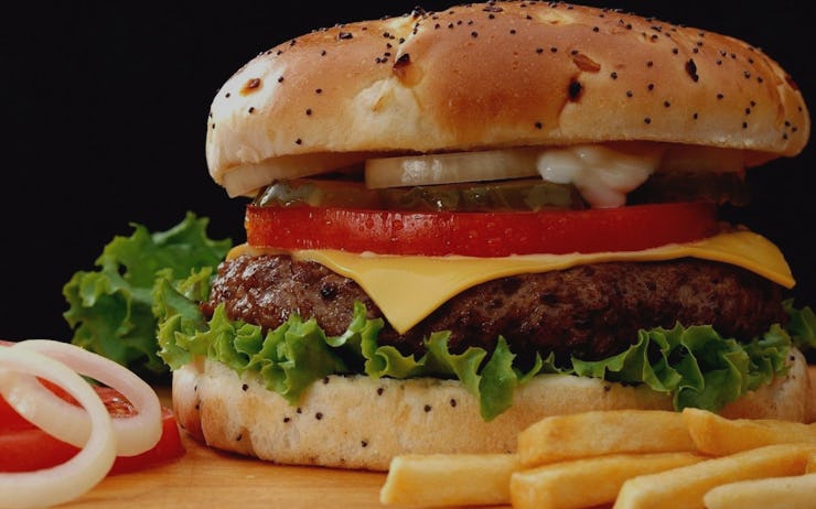 A burger with French fries and tomatoes with onions on the side